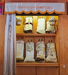 Torah scrolls in an Ashkenazi synagogue Ark (Aron HaKodesh) with the parochet drawn to one side to enable access. The Ark also has solid doors but these are folded back out of the way before the service begins.