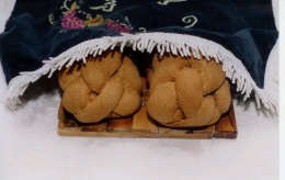 2 loaves of challah partially covered by a challah cloth